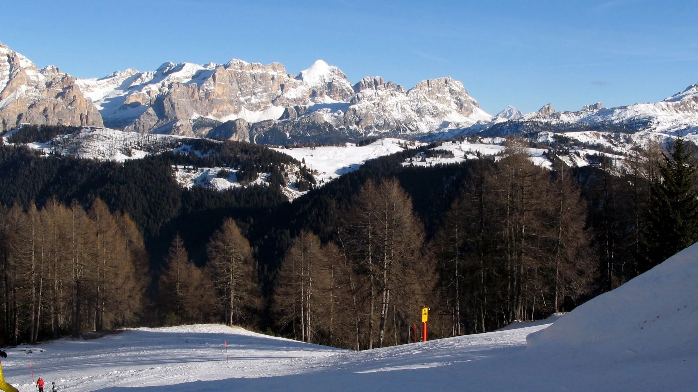 A snowy piste above Colfosco with the Dolomites across the valley