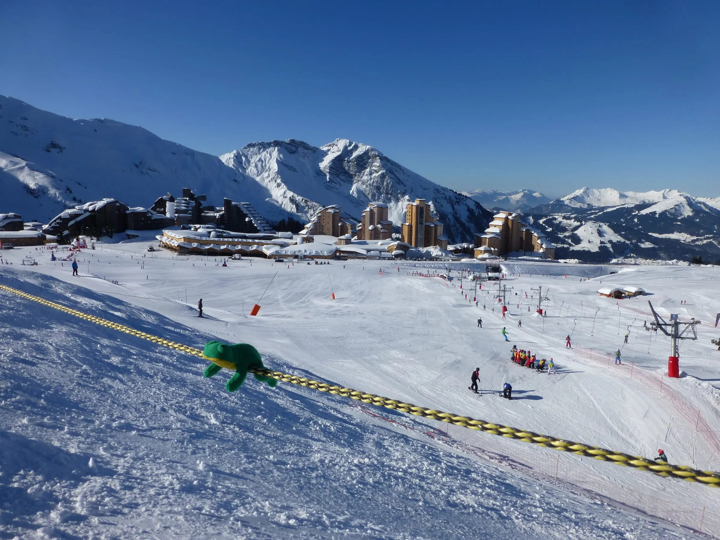 A fenced children's learning area with a small lift and a frog mascot on the snow above Avoriaz