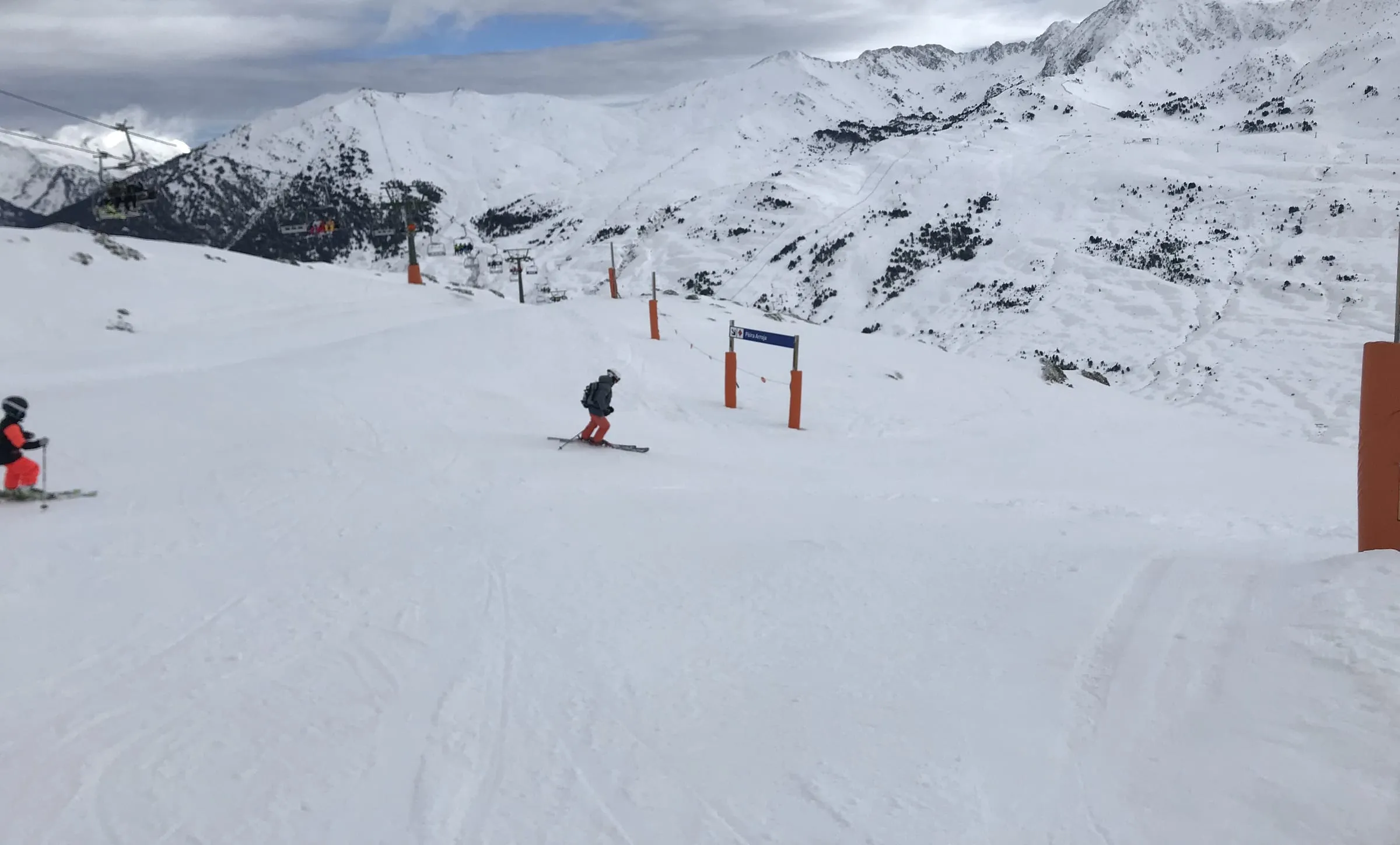 A skier on a wide, groomed piste at Baqueira-Beret with snowy Pyrenean peaks behind