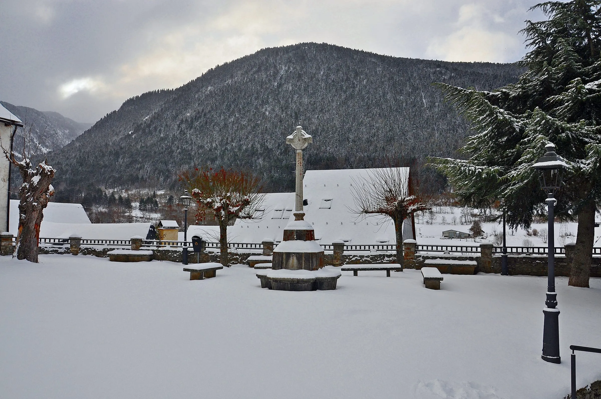 A snowy square with a stone cross in the old centre of Salardú, Val d'Aran