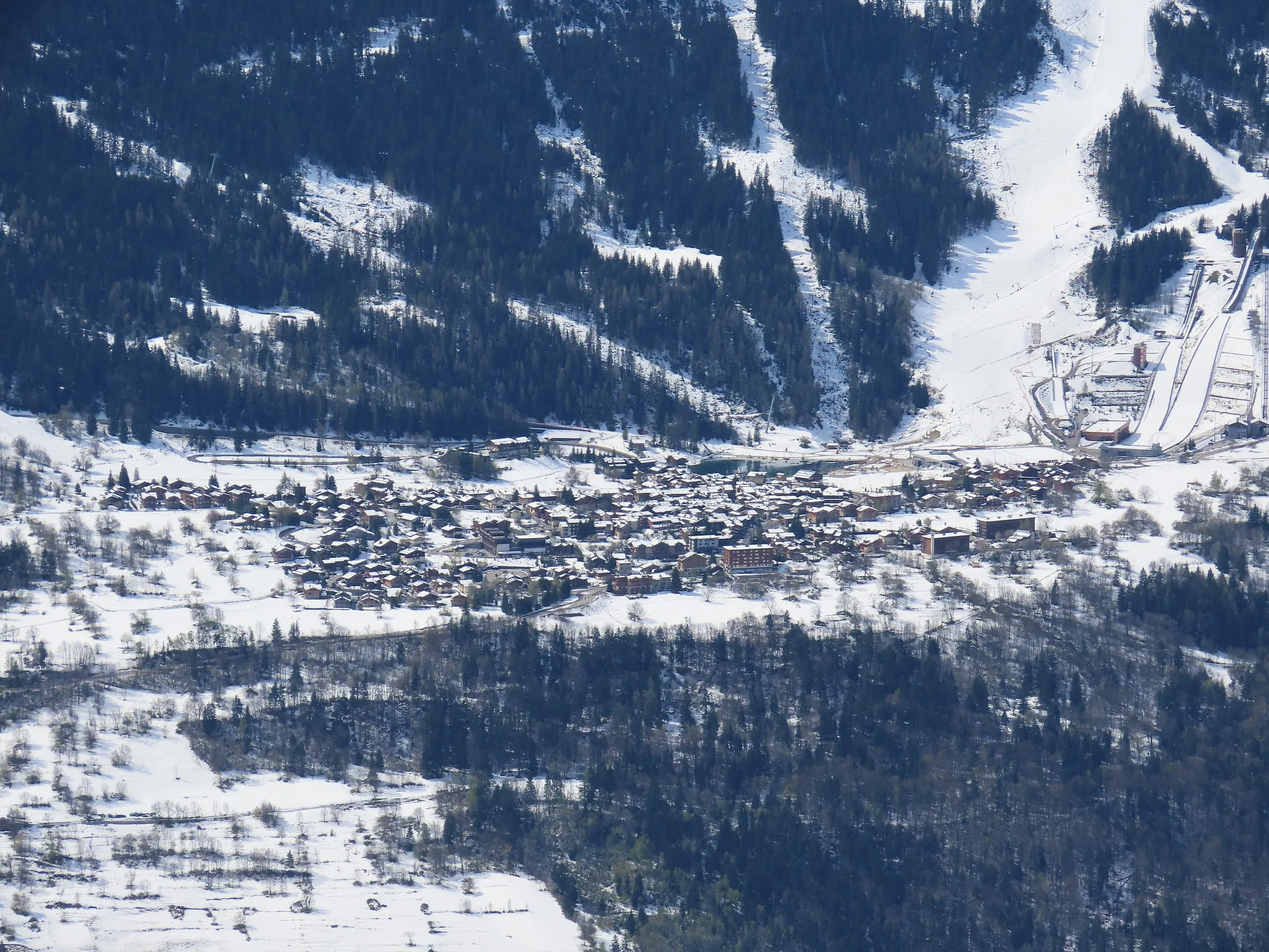 Courchevel Le Praz in the snow, with ski runs cutting through the forest above