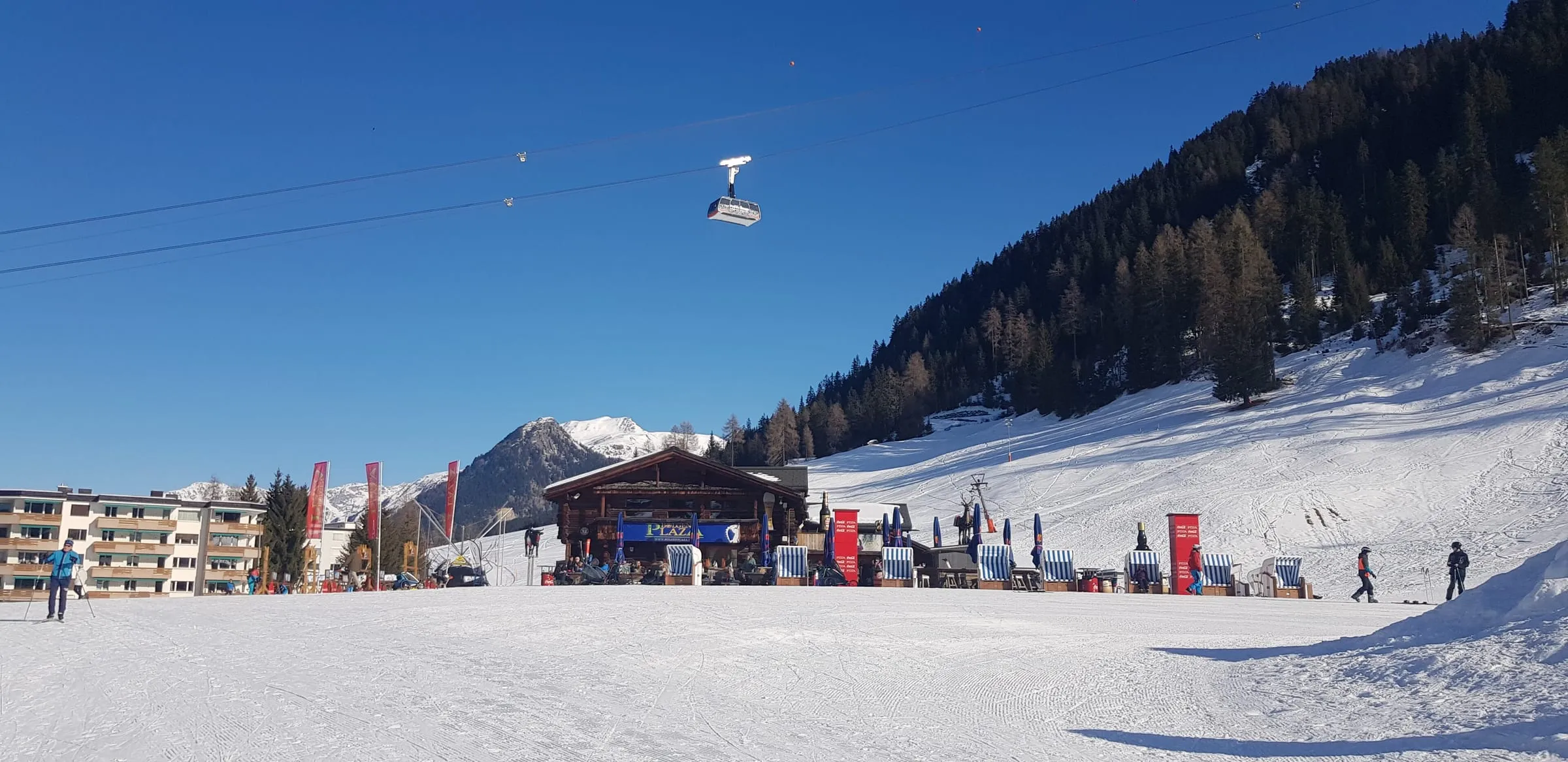 Skiers at the foot of a sunny piste in Davos, with a gondola overhead