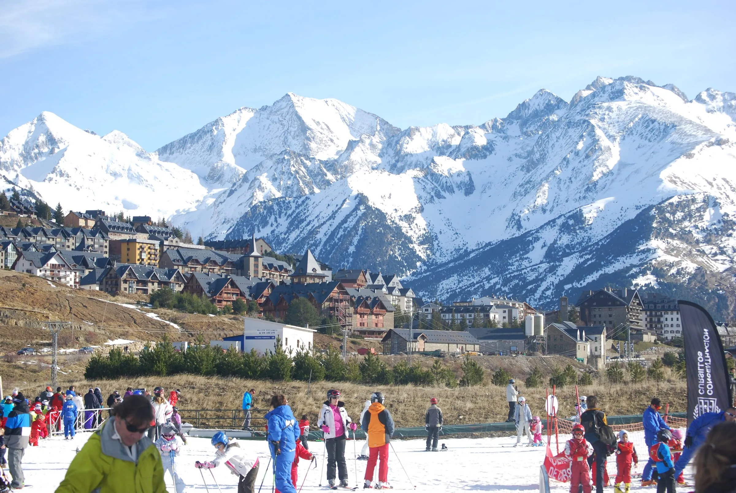 Skiers and children at the foot of the slopes with the Formigal village and snowy peaks behind
