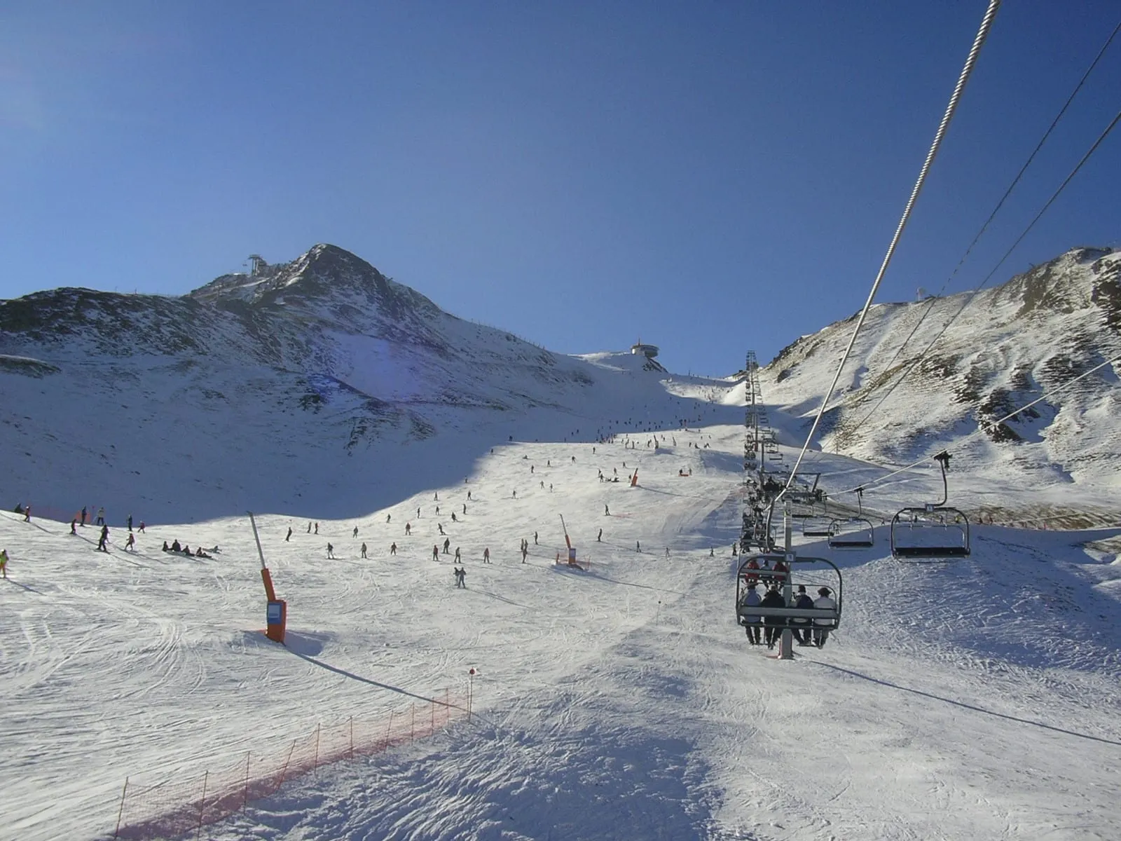 Skiers on wide open pistes in the Pas de la Casa sector of Grandvalira, beside a chairlift