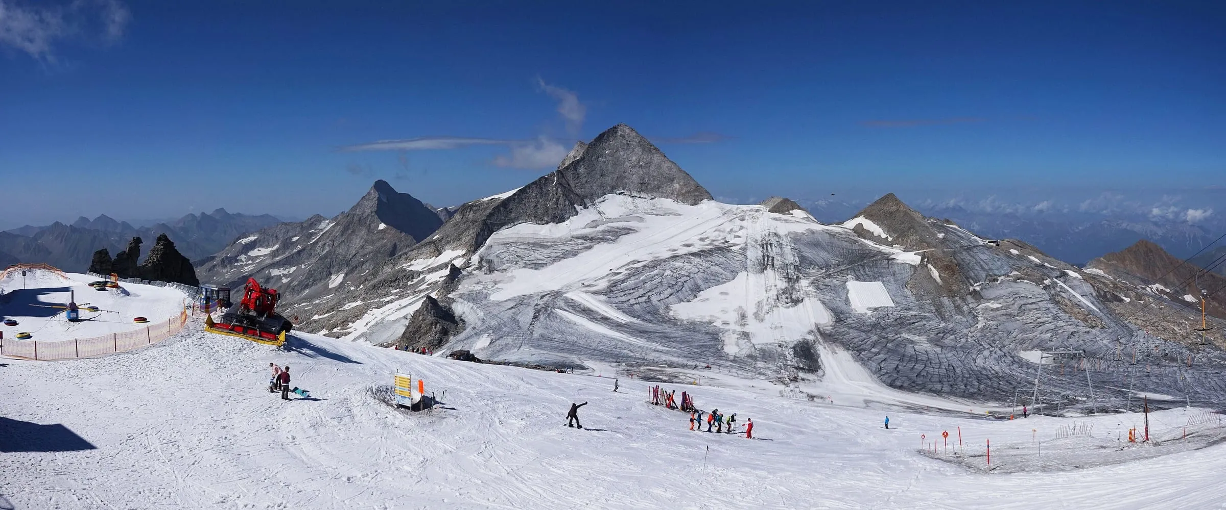Skiers on a snow-covered slope of the Hintertux Glacier in summer, with protective fleece on the ice behind