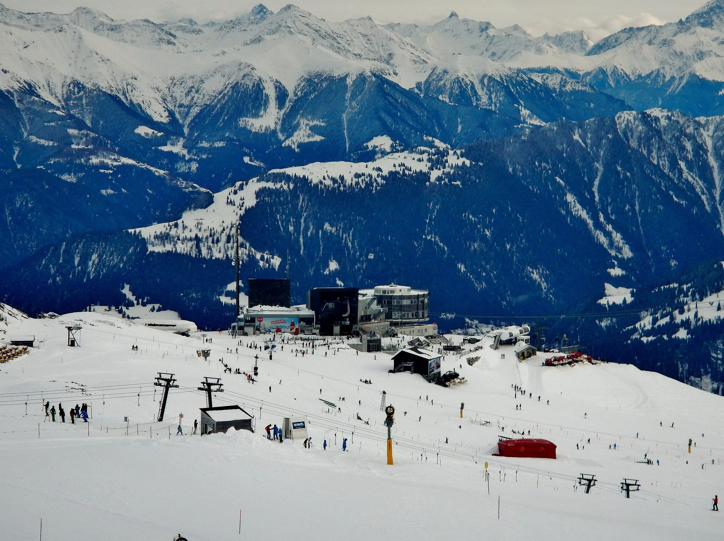 Skiers and lifts on the snowy slopes at Crap Sogn Gion above Laax, with mountains behind