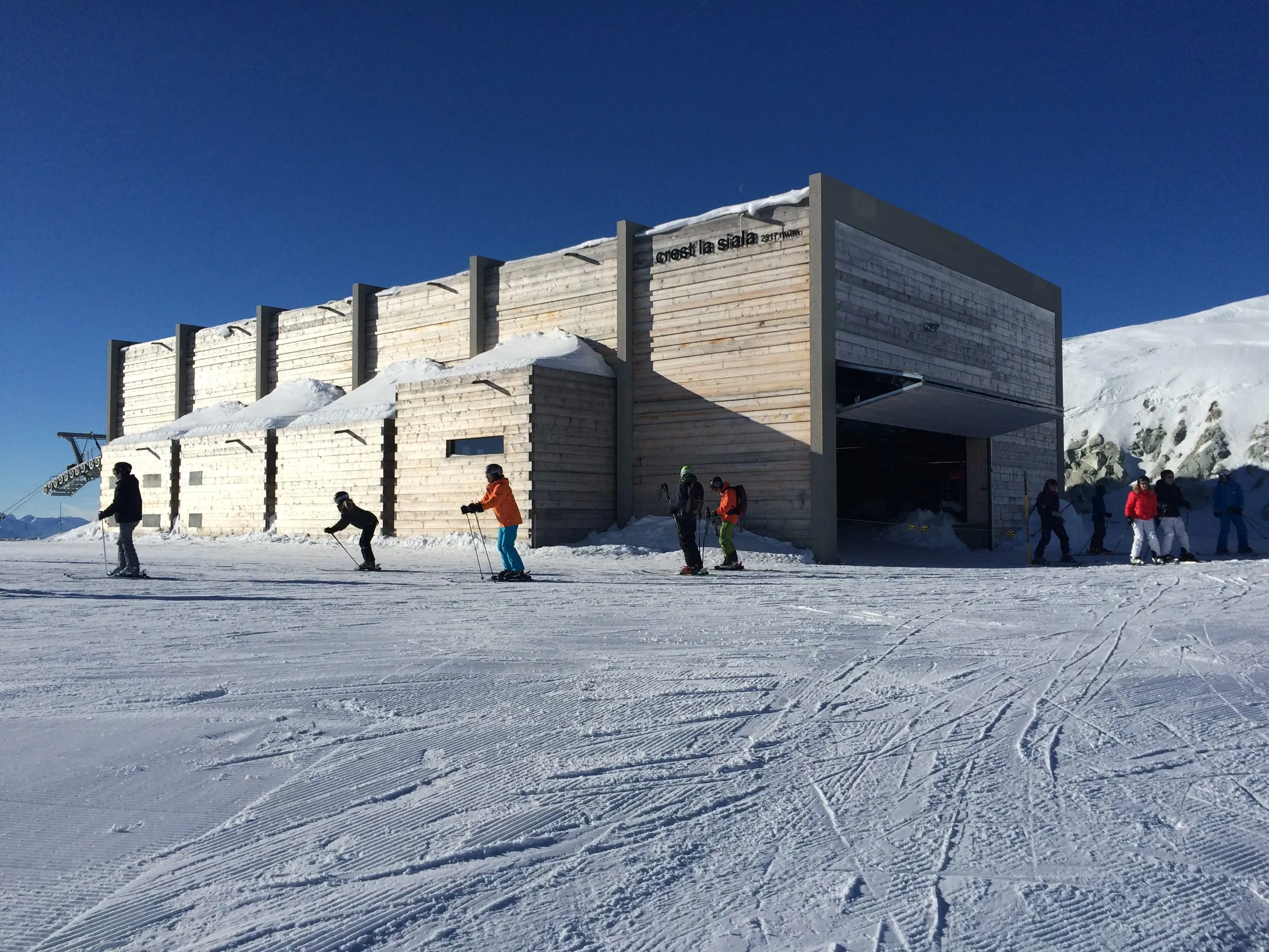 Skiers below the concrete Crest la Siala lift station in the Laax ski area