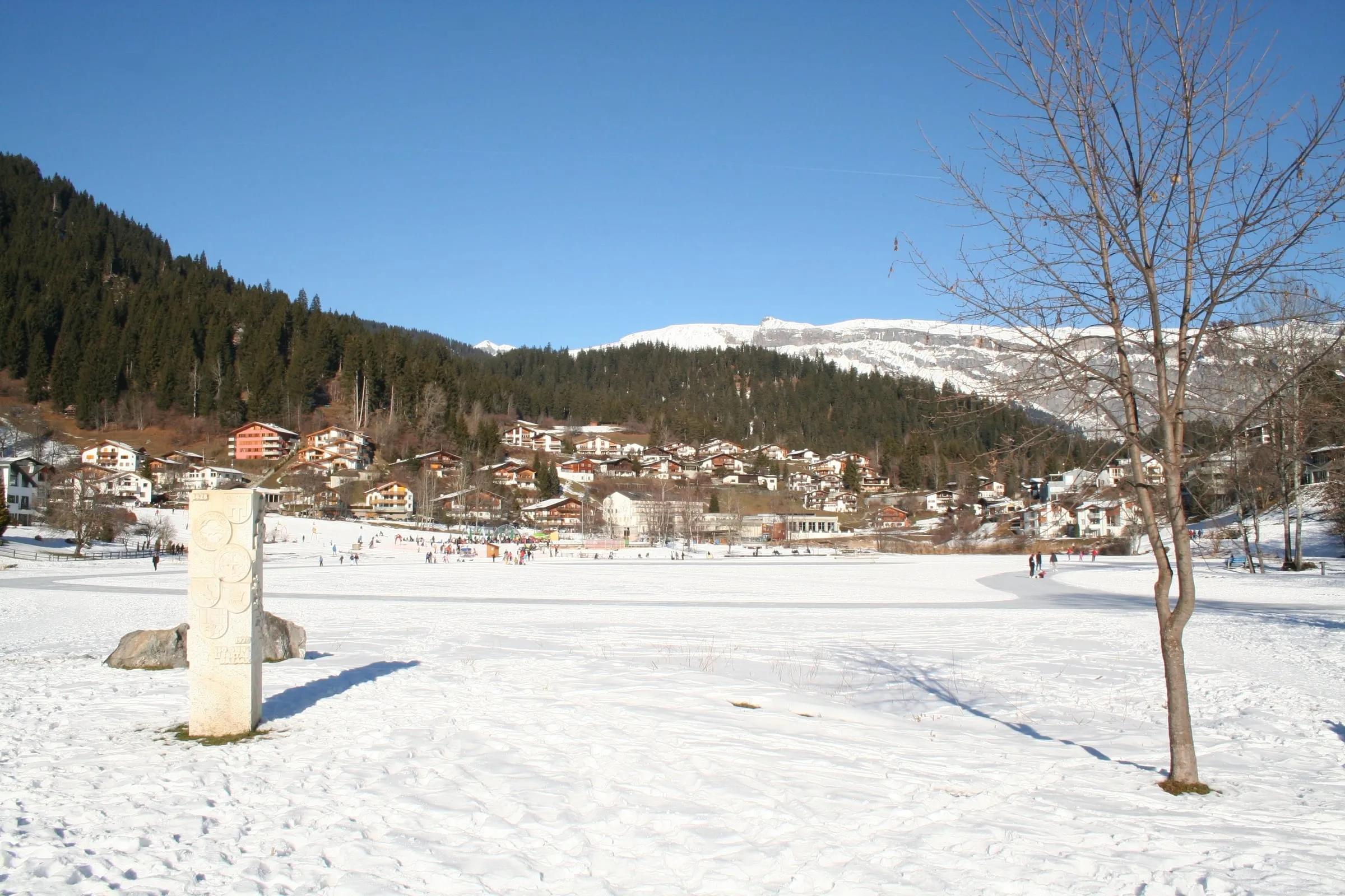 The snow-covered shore of Lake Laax, with the village on the hillside behind