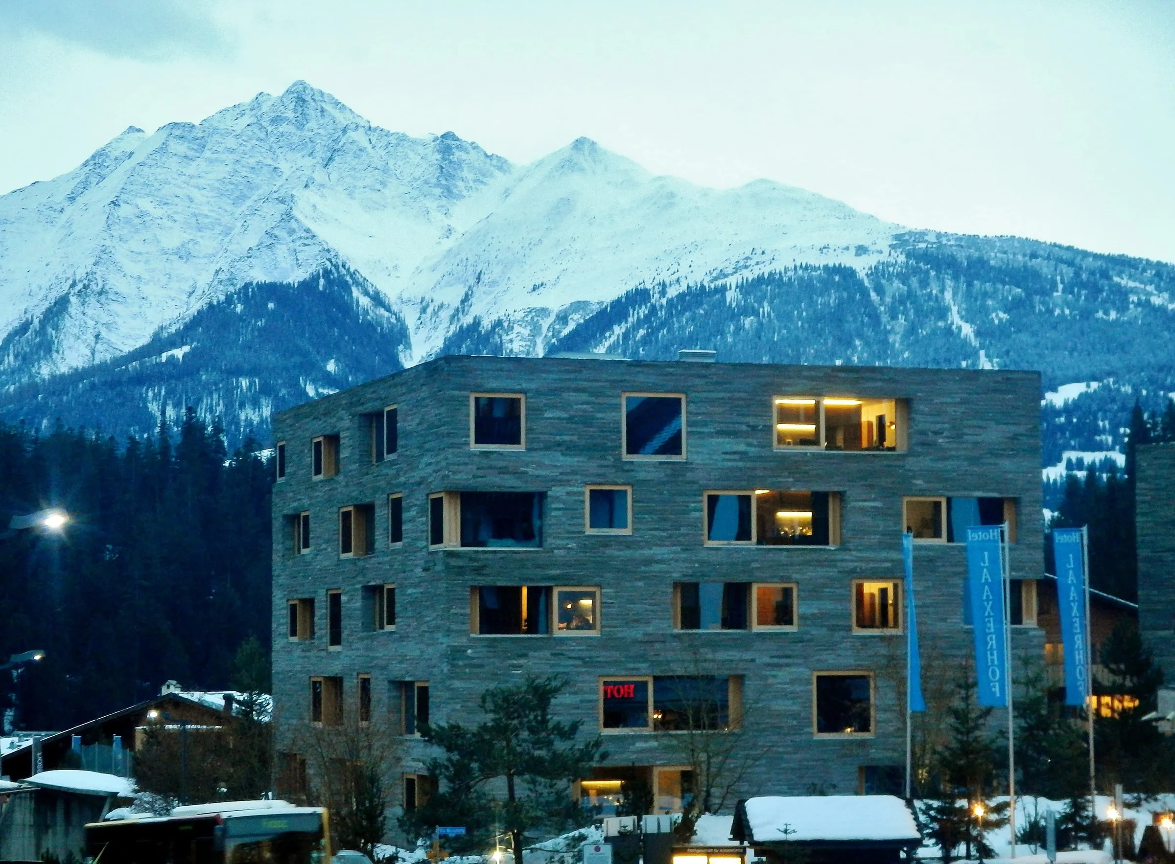 The stone-clad rocksresort buildings at the Laax valley station in winter, with snowy peaks behind