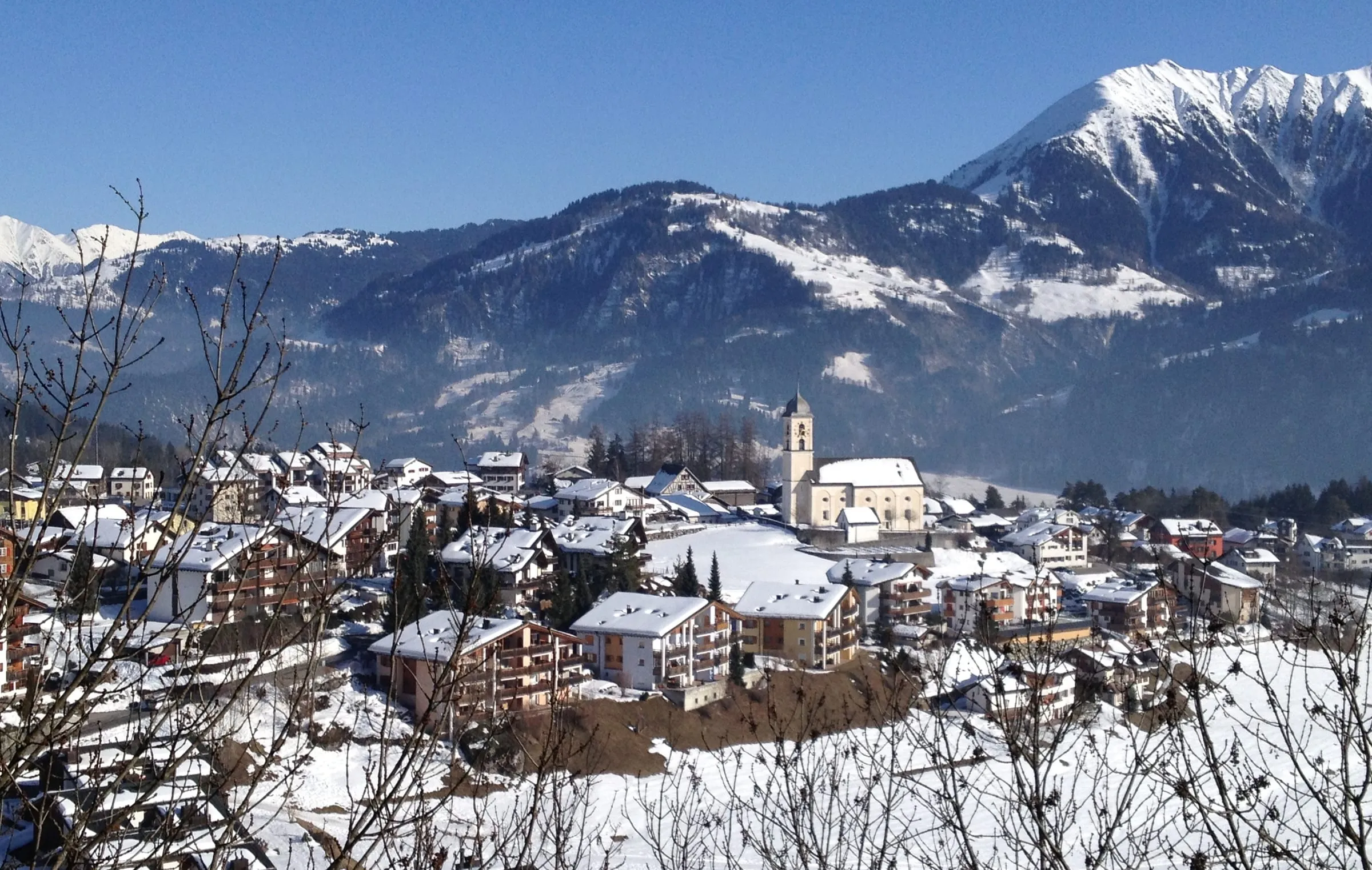 Laax village in winter snow, with its church and the snow-covered mountains of the Surselva behind