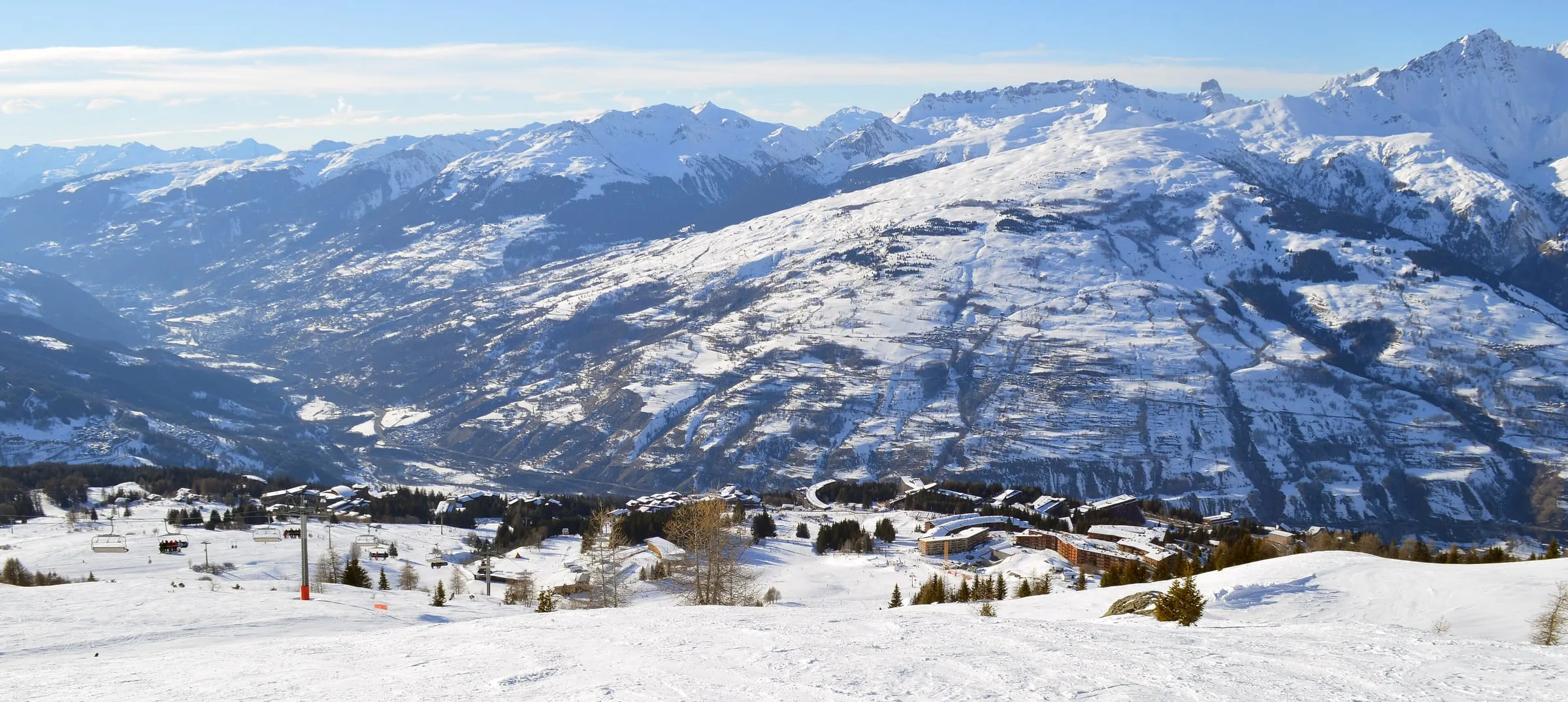 Panoramic view down over Arc 1800 in the snow, with the Tarentaise peaks across the valley