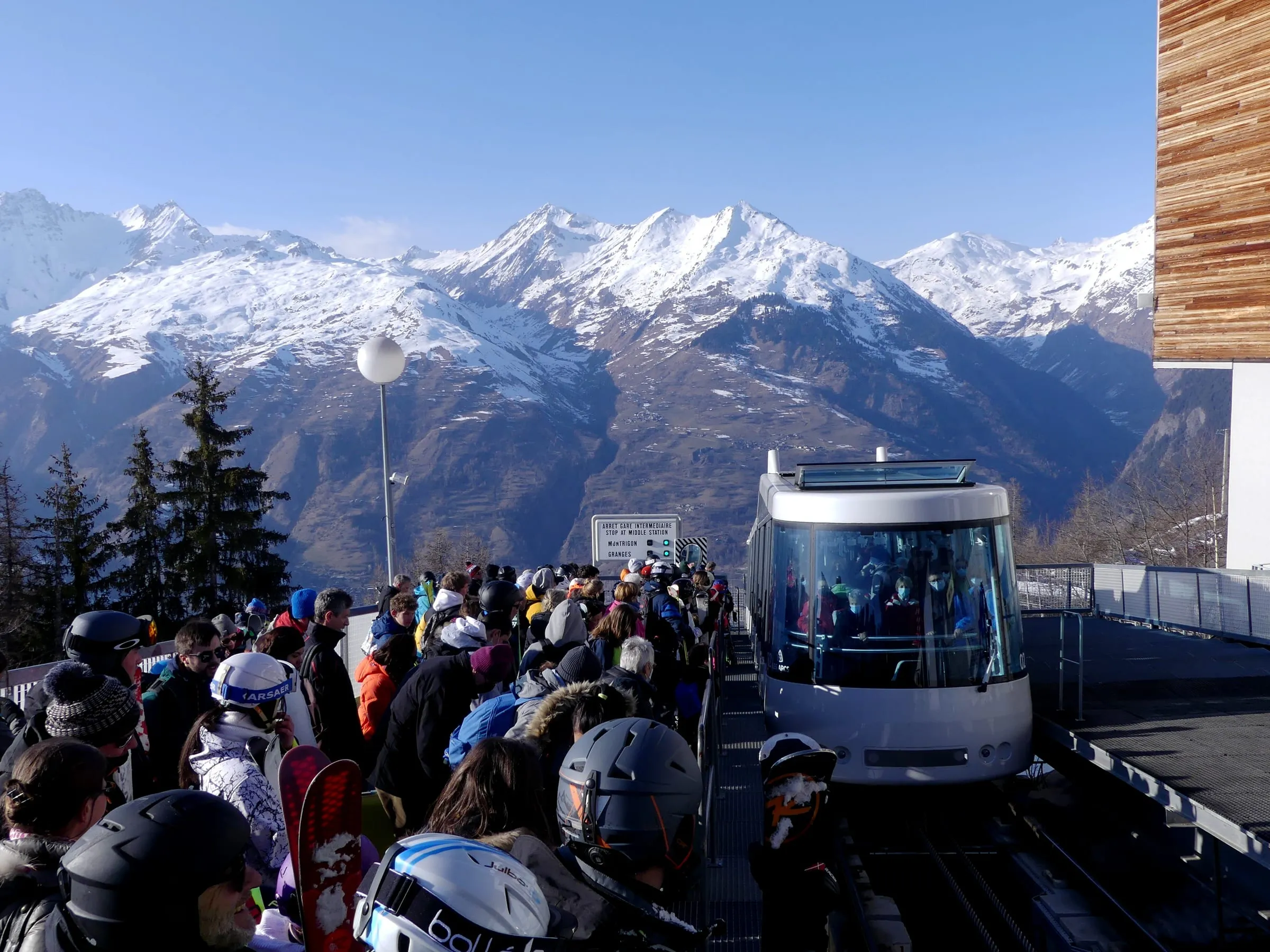 Skiers waiting to board the Arc-en-Ciel funicular at Arc 1600, with snowy peaks behind