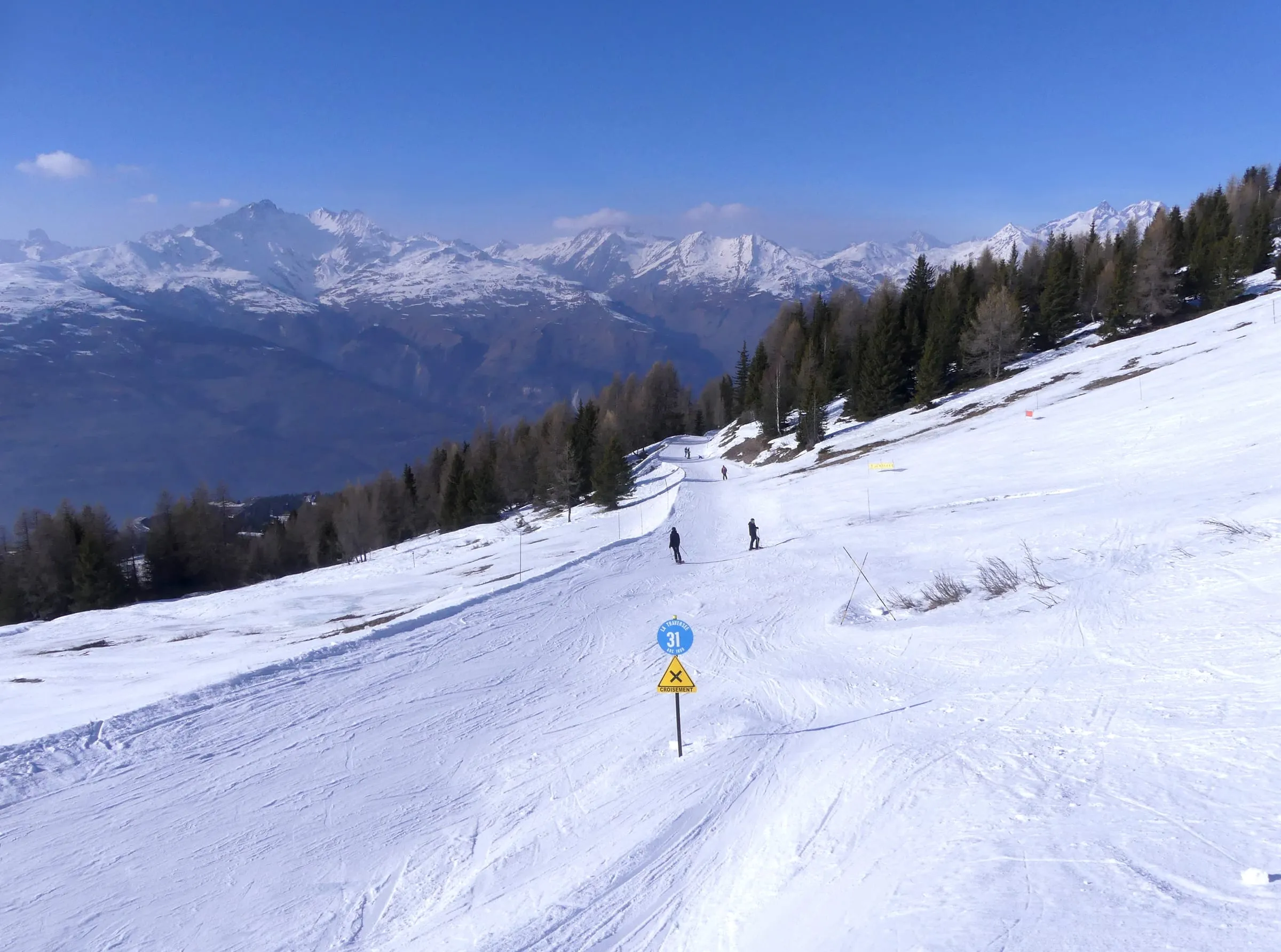 The La Traversée ski run through the trees towards Arc 1600, with mountains behind