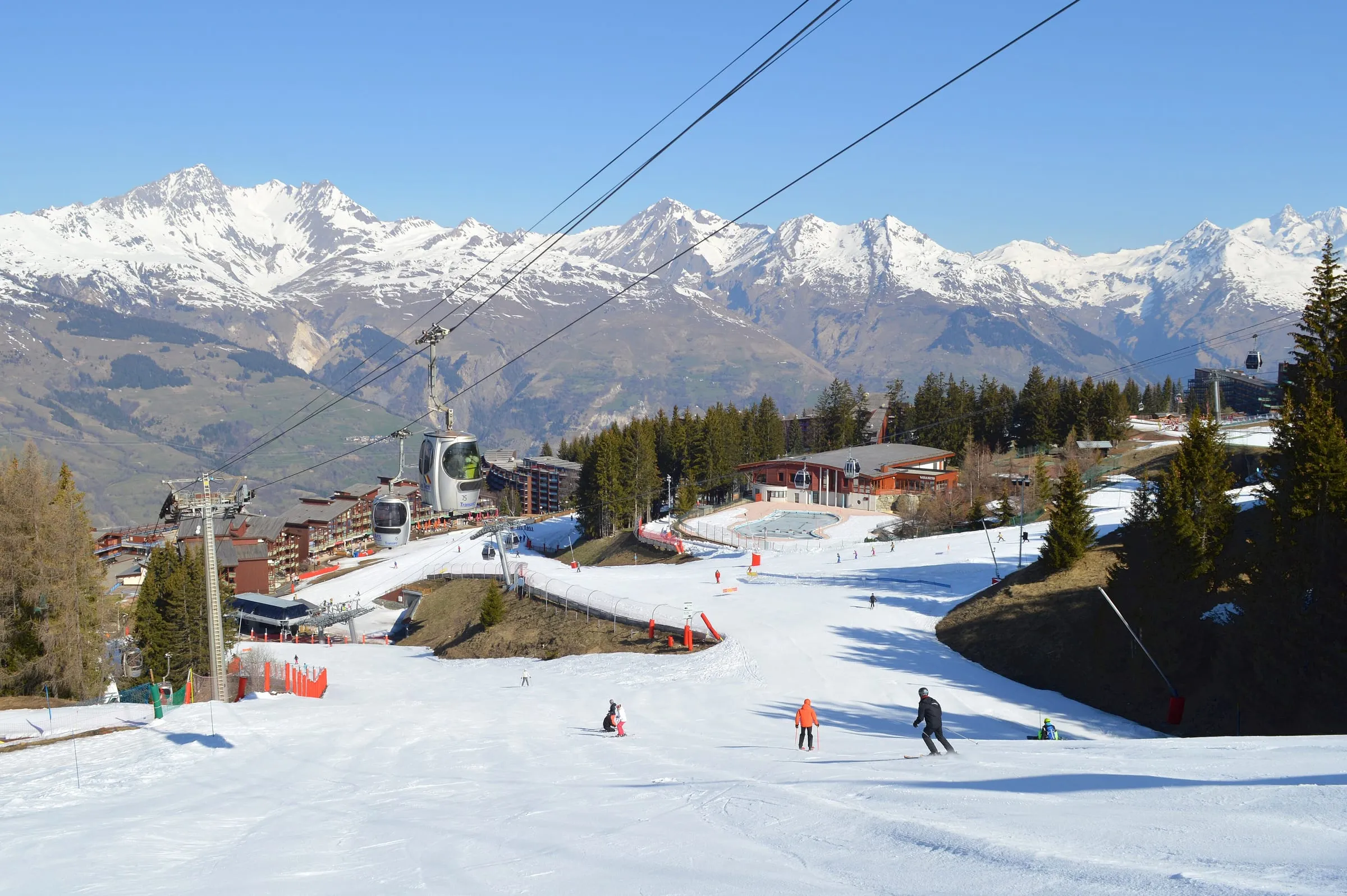 Skiers on a gentle piste at Les Villards in Arc 1800, with snowy peaks behind