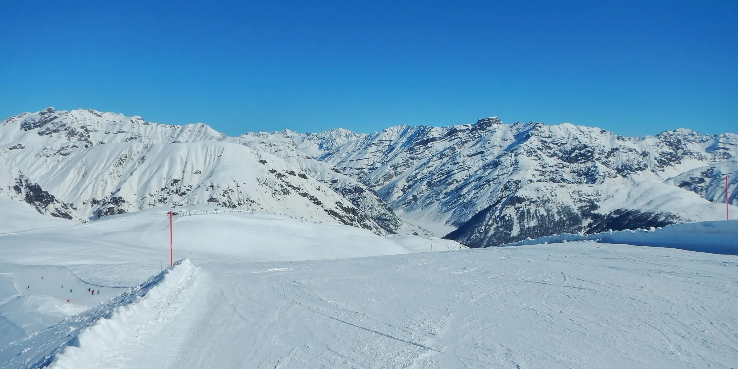 Wide, groomed piste above Livigno with snowy peaks behind