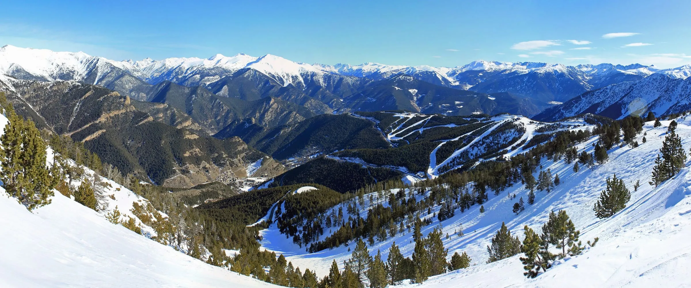 The Pal ski area in winter, with pistes cut through the pine forest and snowy Pyrenean peaks behind