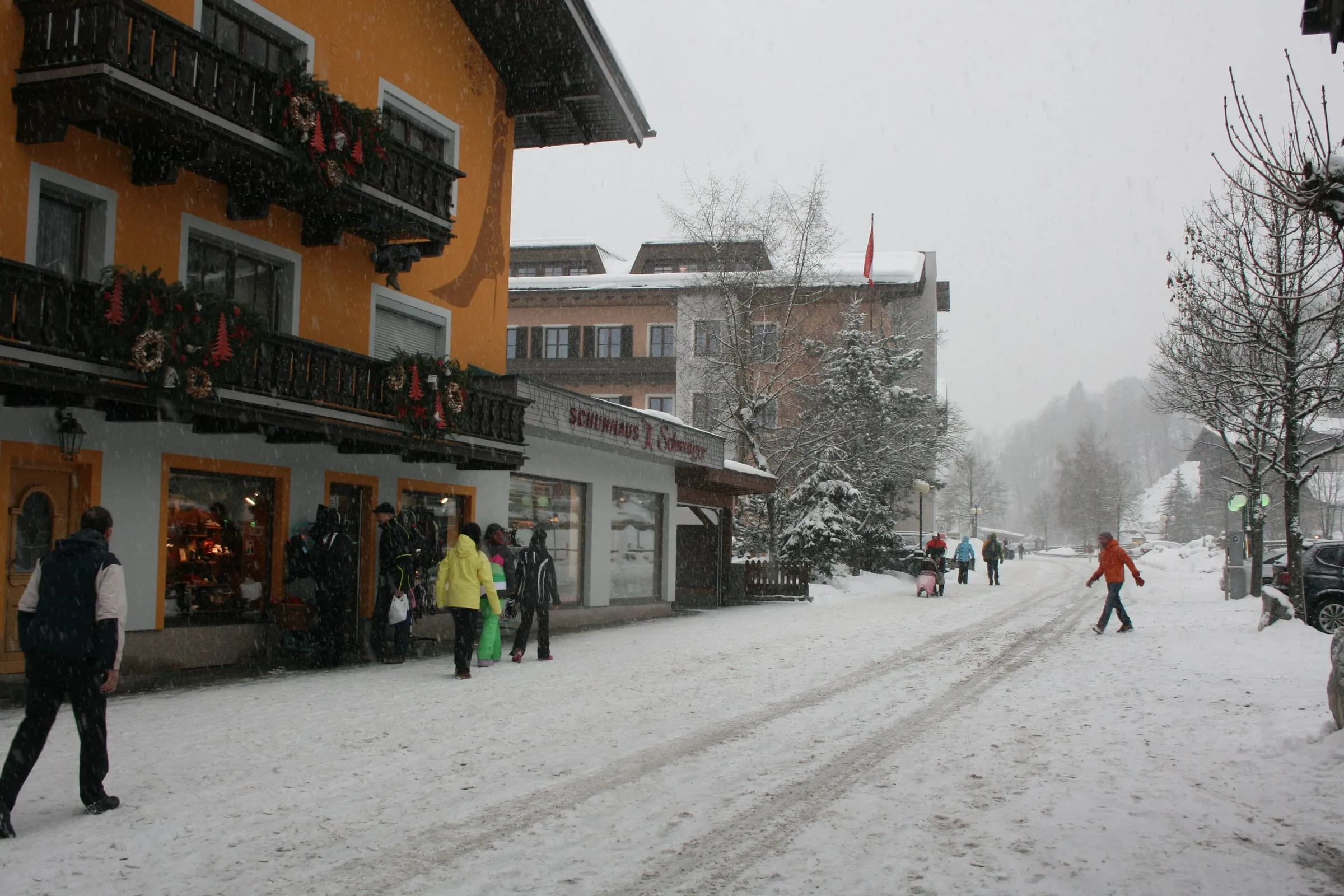 Hinterglemm main street in falling snow, with skiers walking past hotels