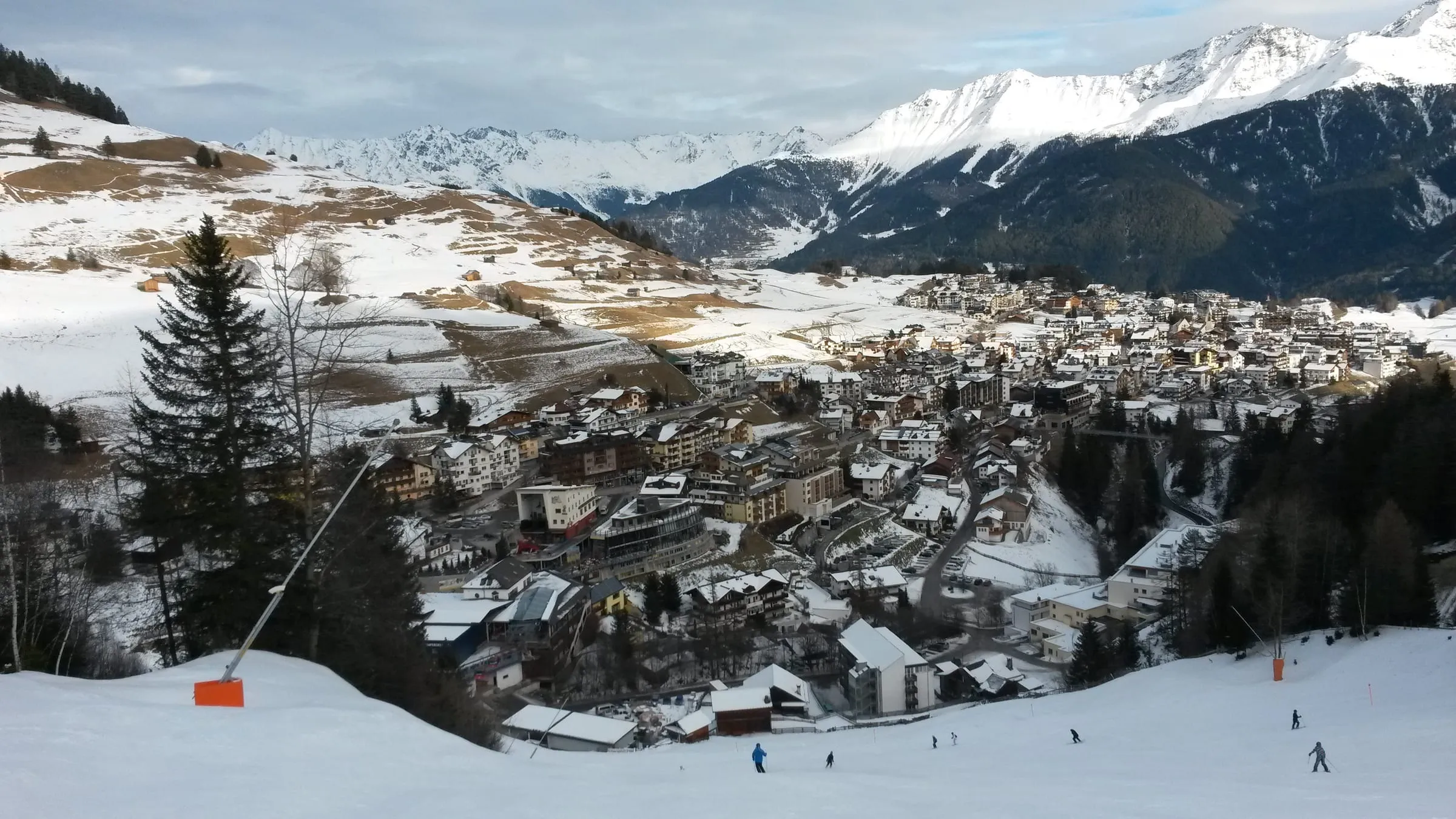 Serfaus village in winter, seen from a piste above, with snowy peaks behind