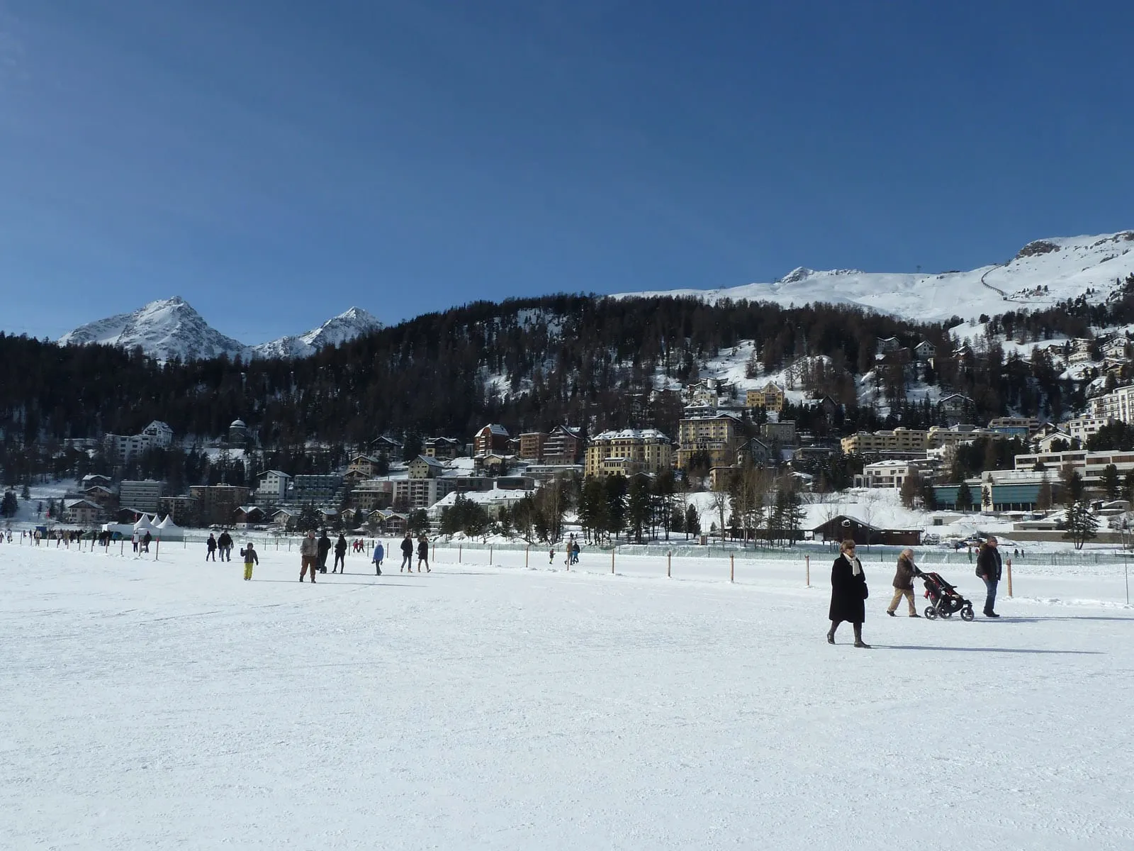 St. Moritz seen across the frozen, snow-covered Lake St. Moritz, with people walking on the ice